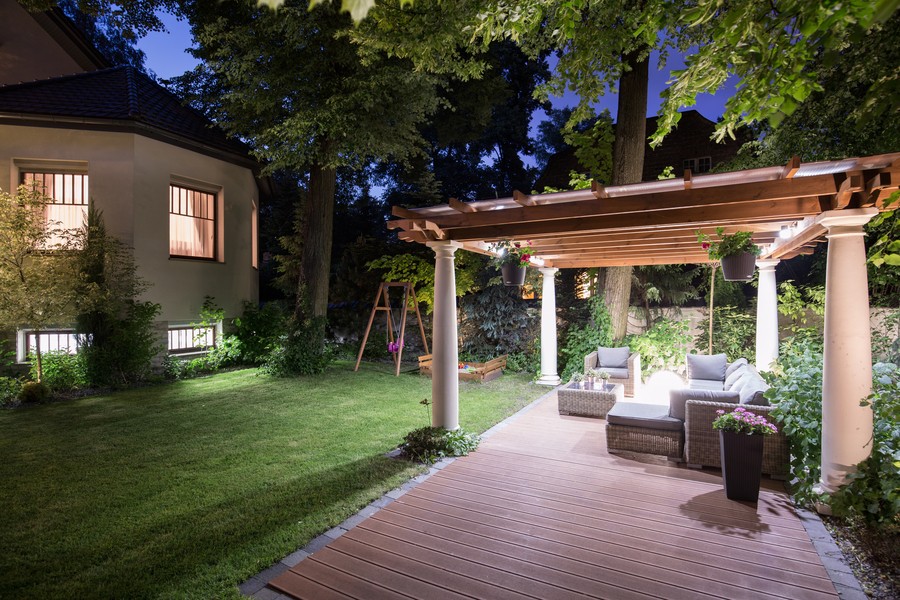 A pergola with expansive sofa seating in a large backyard with custom lighting.